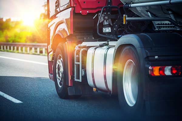 The front wheels of a red semi tractor traveling down the interstate.